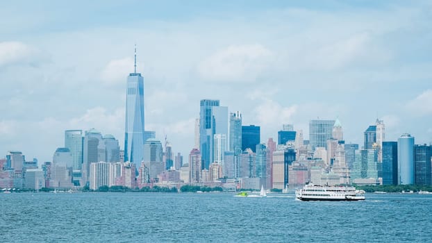 A daytime establishing shot of the lower Manhattan skyline from across the Hudson River in New Jersey. Clear blue sky with white clouds and a white boat on the river in the foreground.