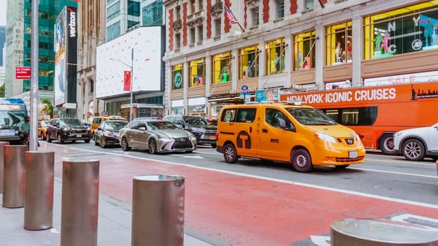 A yellow taxi cab drives through a busy city street with skyscrapers and office buildings in the background. Taxi cab is centered, background slightly blurred. Low angle shot, focused on taxi cab.