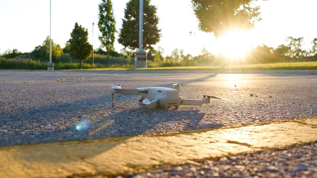 A small consumer quadcopter drone hovers gracefully over the city streets, capturing stunning aerial views as the sun sets in the background, casting a warm orange glow over the urban landscape.