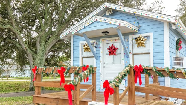 Discover a picturesque small blue cottage adorned with a welcoming wreath, twinkling Christmas lights, and surrounded by two lovely palm trees in the yard, creating a cozy holiday retreat.