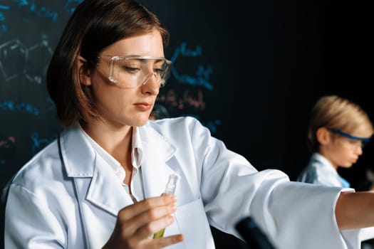 Teacher support schoolboy learning science of chemistry do experiment in laboratory wear lab coat and safety glasses in STEM class. Teacher manage test tube on the table with confidence. Erudition.