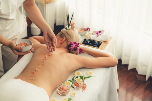 Woman customer having exfoliation treatment in luxury spa salon with warmth candle light ambient. Salt scrub beauty treatment in health spa body scrub. Quiescent