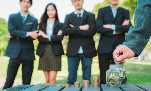 Businessman put coin to money saving glass jar on outdoor table with coin stack as sustainable money growth investment or eco-subsidize for corporate promoting environmental awareness. Gyre