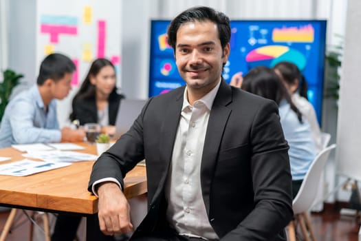 Portrait of businessman or analyst looking at camera with his colleague analyzing data analysis in dynamic business strategy investment planning meeting. Meticulous