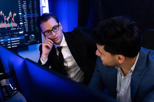 Two stock exchange traders discussing digital currency or market online focusing on dynamic data monitor. Concept of analyzing market stock cooperate at neon blue-light decorative workplace. Sellable.