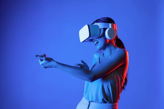 Smart female standing wearing VR headset connecting metaverse, future cyberspace community technology. Elegant woman using hands commanding virtual gun seriously playing shooting games. Hallucination.