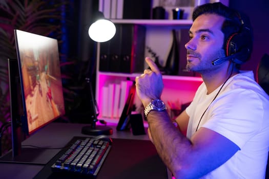 Smart gaming streamer enjoy playing battle team with streaming online shooting gun game with multi or single player at warship on pc screen, wearing headset at digital neon light cyber room. Surmise.