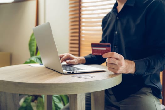 Young man using laptop with credit card for internet banking, online shopping E commerce by online payment gateway at home office. Modern and convenience online purchasing with debit card. Unveiling
