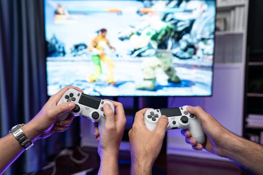Friend gamers playing video game of battle martial arts fighter on TV using joysticks position of backside background. Comfy living neon light at home place with cheerful fighting winner. Sellable.