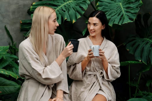 Tropical and exotic spa garden with bathtub in modern hotel or resort with young two women in bathrobe drink coffee, enjoy leisure and wellness lifestyle surround by lush greenery foliage. Blithe
