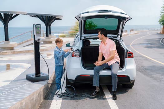 Family road trip vacation traveling by the sea with electric car, father and son recharge EV car with green and clean energy. Natural travel and eco-friendly car for sustainable environment. Perpetual