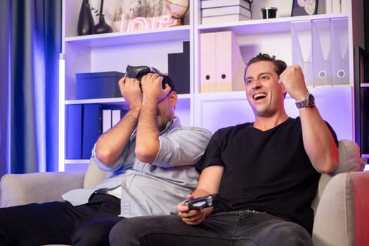 Winner and loser players of buddy friend gamers playing video game on TV using joysticks in studio room with neon blue light. Comfy living indoor at home place with cheerful fighting winner. Sellable.