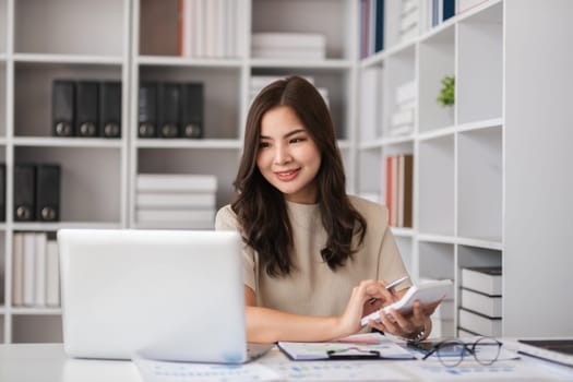 Young female accountant working from home, using a laptop and calculator in a modern home office environment.