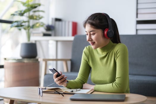 Asian woman checking smartphone while working with headphones in modern office, concept of connectivity.