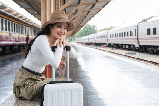 Asian woman waiting at train station with suitcase, concept of travel anticipation.