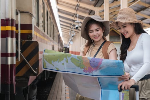 Asian women travelers with map at train station, concept of adventure.