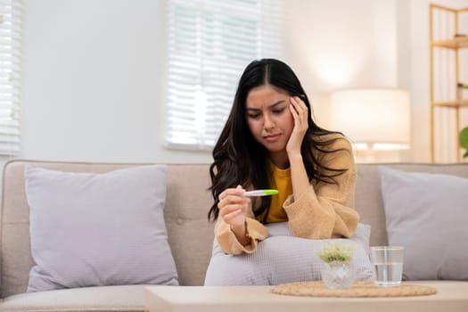 A young woman sitting on a couch, holding a pregnancy test with a worried expression, in a bright and cozy living room.