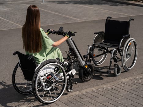 Woman in wheelchair with assistive device for manual control next to classic wheelchair. Electric handbike