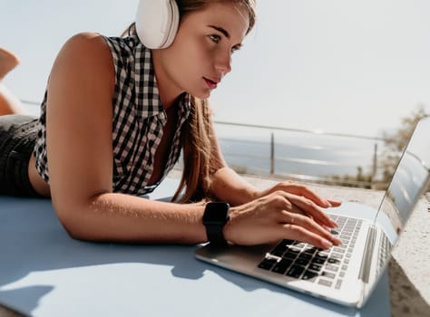 Digital nomad, Business woman working on laptop by the sea. Pretty lady typing on computer by the sea at sunset, makes a business transaction online from a distance. Freelance, remote work on vacation