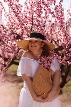 Woman blooming peach orchard. Against the backdrop of a picturesque peach orchard, a woman in a long white dress and hat enjoys a peaceful walk in the park, surrounded by the beauty of nature