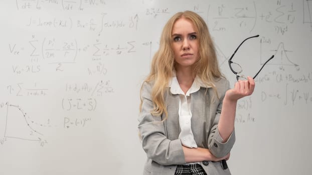 A Caucasian woman stands at a blackboard with written formulas