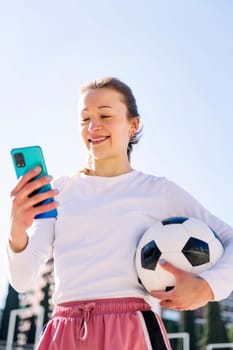 smiling young woman holding a soccer ball while using mobile phone, concept of technology of communication and social media, copy space for text