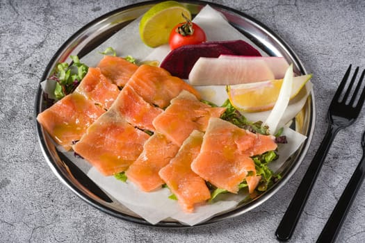 Smoked salmon with greens under it on a stone table