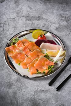 Smoked salmon with greens under it on a stone table