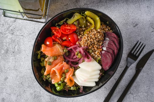 Healthy salad with quinoa, capers and salmon in black bowl