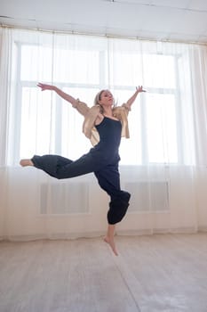 Caucasian woman dances contemporary in ballet class. Dancer in a jump. Vertical photo