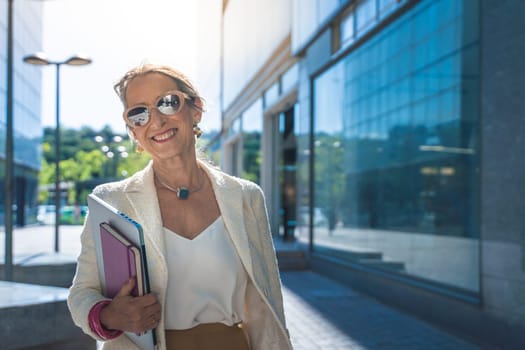 Middle-aged Caucasian business woman looking at camera. Beautiful mature lady smiling with sunglasses, books and tablet. High quality photo