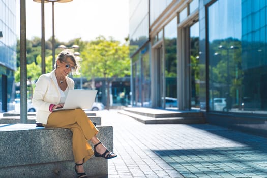 Happy attractive business woman middle-aged working smiling with laptop in front of a modern building. High quality photo