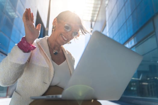 Video call of a happy attractive business woman middle-aged smiling with laptop in front of a modern building. High quality photo