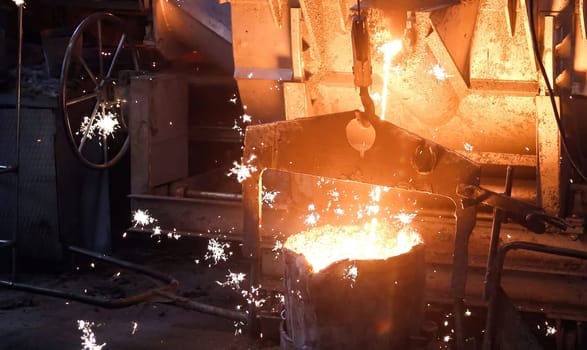 Molten metal poured from ladle into mold to make casting. Metal glows brightly, flows into mold, sparks fly as metal hits mold, on dark background, showcasing metal casting process.