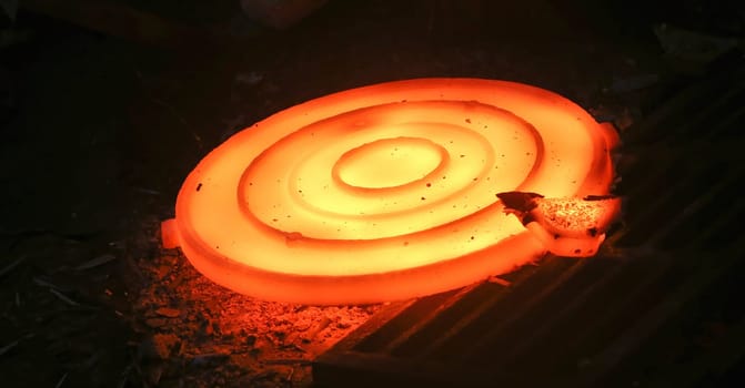 Industrial metalworking or manufacturing concept. Glowing hot round metal disc forging press isolated on black background. Industrial concept of power, energy, and strength.