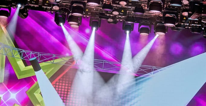 Vibrant purple stage lights and bright rays create an energetic atmosphere, perfect for concerts. The colorful lights draw audience attention to the stage, enhancing excitement and anticipation.