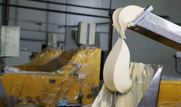 A large portion of uncooked dough flows from a metal chute into a processing container at an industrial bakery. The equipment is designed for high-volume production, facilitating the efficient preparation of dough for subsequent baking stages.