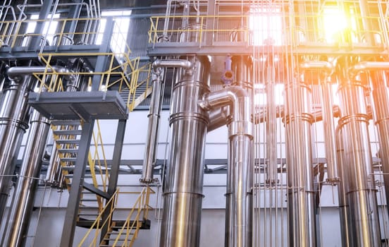 A chemical plant features a complex network of stainless steel pipes and glass vessels, creating an intricate system of interconnected straight and curved components in various sizes and shapes.