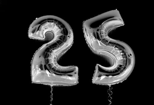 Two silver mylar number balloons forming the number 25 on a black background. The balloons are shiny and reflective, and the black background makes the numbers stand out.