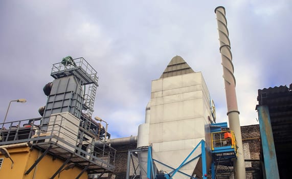 A view of a large industrial complex featuring tall structures, including a tall exhaust stack.