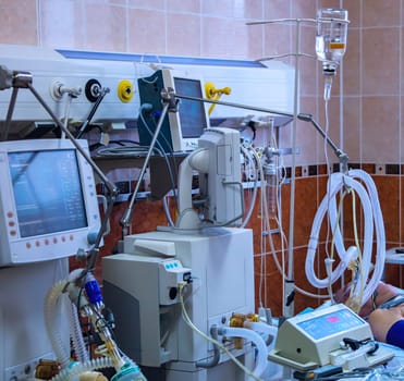A close-up view of medical equipment in a hospital operating room, featuring a monitor displaying medical data, a respirator, a drip, and tubes connected to the equipment.