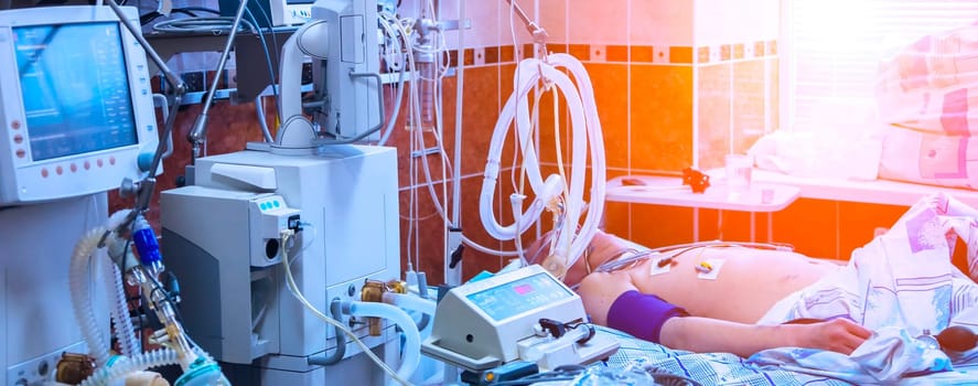 A patient lies in a hospital bed, connected to life support equipment. The room is brightly lit, with a window behind the patient.