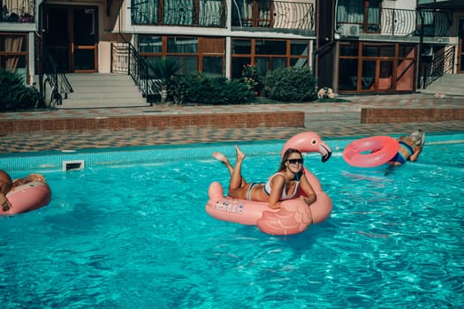 A woman is floating in a pink flamingo float in a pool. The pool is surrounded by a brick wall and has a few other people in the background