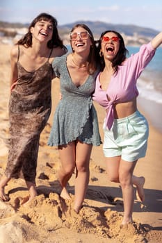 Cheerful multiethnic friends with sunglasses happy on vacation on the beach, looking at the camera.