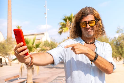 A happy man is inside the university campus taking a self-portrait with a cell phone.