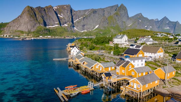 An aerial view of colorful wooden houses on stilts in a picturesque village in the Lofoten Islands, Norway, with majestic mountains in the background. Sakrisoy, Lofoten, Norway