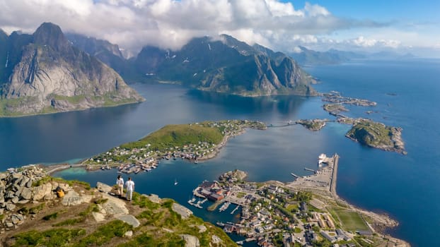 An aerial view of a Norwegian fjord, showing a small town nestled between the mountains and the water. a couple of men and women at Reinebringen Lofoten Norway