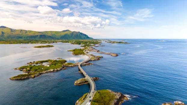 A picturesque aerial view of the Atlantic Road in Norway, showcasing a winding bridge connecting small islands amidst stunning blue waters and a backdrop of rolling hills.