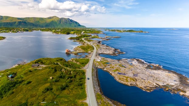 An aerial view of a winding road cutting through the rugged coastline of Norway, with mountains and islands in the distance. Atlantic Ocean Road Norway