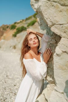 A woman in a white dress is standing on a rocky beach. Concept of serenity and tranquility, as the woman is enjoying the natural beauty of the beach